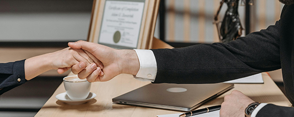 Business handshake across a desk with a laptop