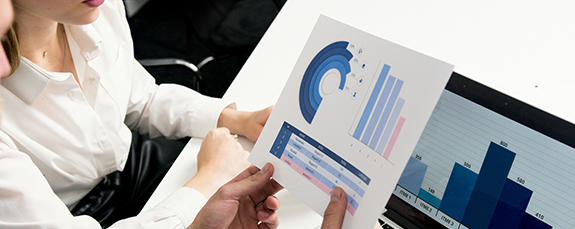 Hands holding printed charts beside a laptop