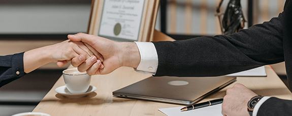 Business handshake across a desk with a laptop